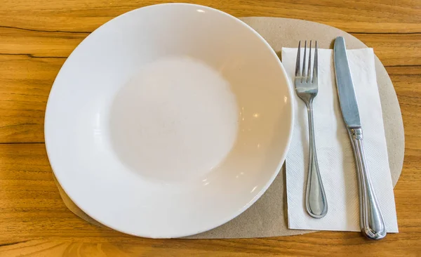 Пустая белая тарелка с ложкой и ножом на деревянном фоне — стоковое фото