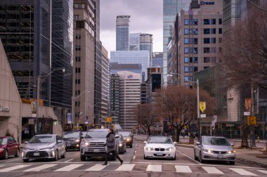 TORONTO, CANADA - 01 04 2020: Richmond Caddesi 'ndeki yaya geçidi boyunca yürüyen bir yaya, arka planda bekleyen arabaların ve yüksek binaların önünde duruyor.