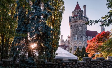 TORONTO, Kanada - 10 09 2018: Casa Loma 'nın yanındaki ağaçların arasından güneş ışıldıyor. Casa Loma Gotik Diriliş Kalesi gibi bir bina. Toronto 'nun en ünlü simgelerinden biri haline geldi.