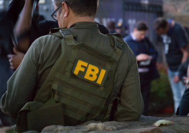 FBI logosu olan yeşil kurşun geçirmez yelek takan beyaz erkek FBI ajanı, olay yerinde arkadan görüldü.
