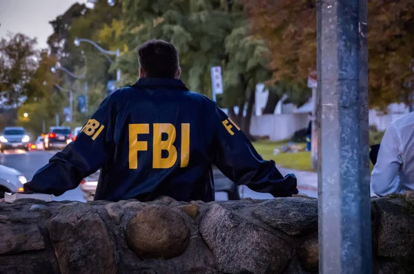 Agente masculino do FBI vestindo casaco azul escuro com logotipo do FBI olhando para a rua com carros no crepúsculo visto por trás — Fotografia de Stock