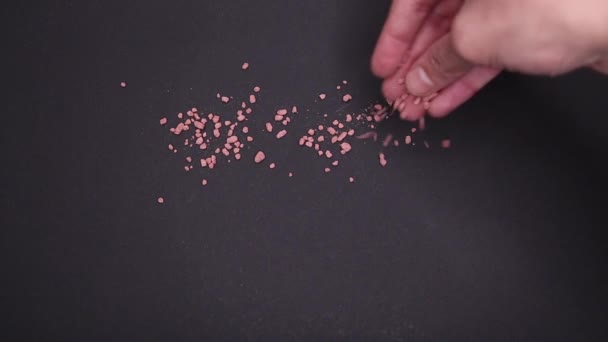 Petits grains roses et jaunes éparpillés sur une table noire avec une main masculine 