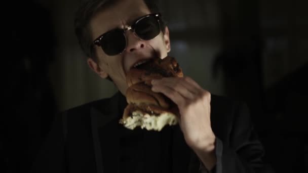 Estilo tipo en gafas negras come rollo. Comer un rollo en una chaqueta en un fondo negro — Vídeo de stock