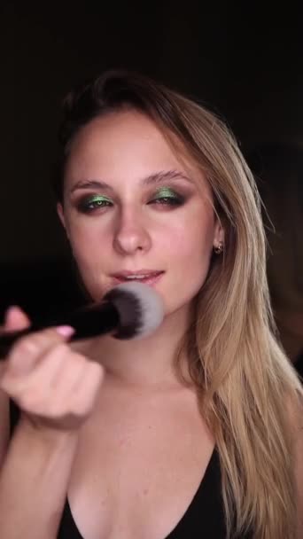 Vacker flicka med gröna ögon gör makeup med en borste på en svart bakgrund. Vertikal video — Stockvideo