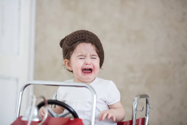 Child crying in red car. Kid in a brown hat — Stock Photo, Image