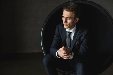 gri arka plan üzerinde sandalyede oturan genç işadamı