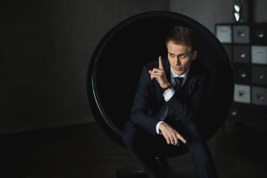 gri arka plan üzerinde sandalyede oturan genç işadamı