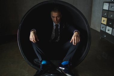 genç işadamı gri arka plan üzerinde sandalyede oturarak poz duygusal