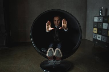 genç işadamı gri arka plan üzerinde sandalyede oturarak poz duygusal