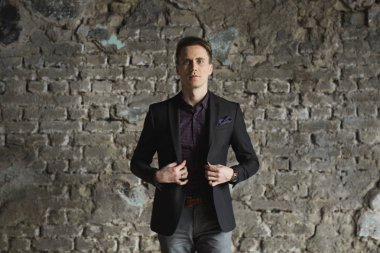 Mutlu gülümseyen yakışıklı adam ayakta ve kameraya gri arka plan üzerinde seyir siyah elbiseli