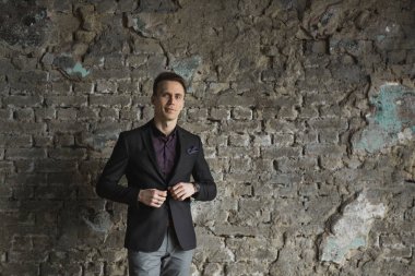 Mutlu gülümseyen yakışıklı adam ayakta ve kameraya gri arka plan üzerinde seyir siyah elbiseli