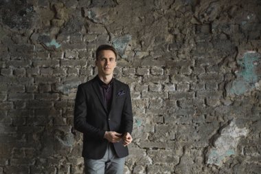 Mutlu gülümseyen yakışıklı adam ayakta ve kameraya gri arka plan üzerinde seyir siyah elbiseli