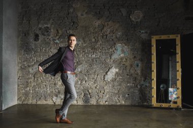 Siyah takım elbise poz ve gri arka plan üzerinde kameraya bakarak duygusal olarak mutlu gülümseyen yakışıklı adam