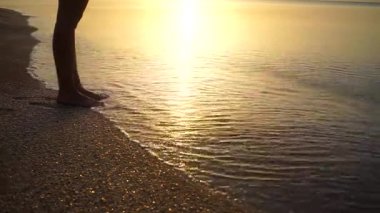 Genç kadın bacakları kuma basıyor. Sahilde altın kumda yürürken arka planda okyanus dalgaları olan kadın ayaklarına yakın dur. Deniz kıyısındaki çıplak ayaklı kız. Yaz tatili. Yavaş çekim