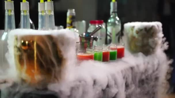 Алкогольные коктейли разных цветов на столе для ругательств в дыму — стоковое видео