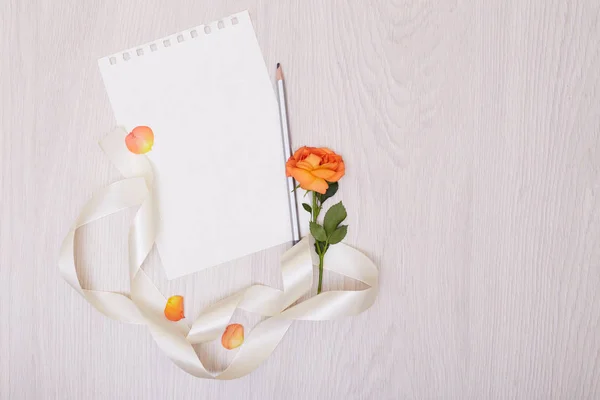 Una maqueta creativa con una tarjeta y una rosa de orang. Hoja vacía de pape — Foto de Stock