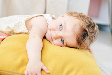 sevimli küçük kız turuncu bir yastık ile oynuyor. Yastığın üzerinde yatıyor