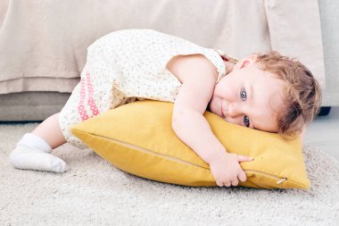 sevimli küçük kız turuncu bir yastık ile oynuyor. Yastığın üzerinde yatıyor