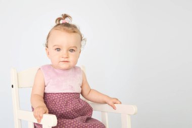 elbiseli güzel küçük kız beyaz bir sandalyede oturur