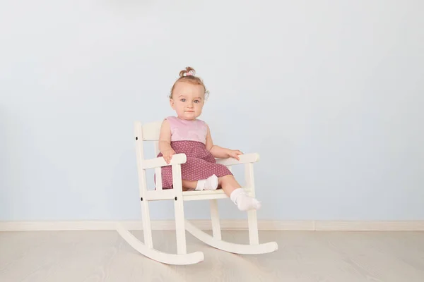 Beautiful little girl in a dress sits on a white chair — Stock Photo, Image