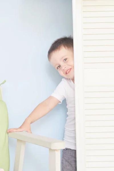 happy kid behind door. the boy plays. He hides behind the white door