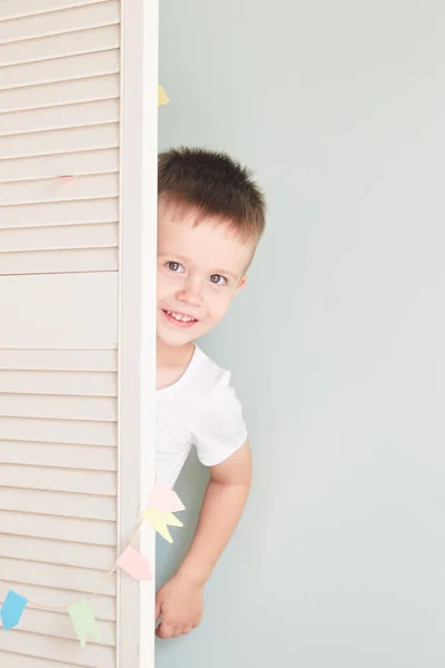 happy kid behind door. the boy plays. He hides behind the white door