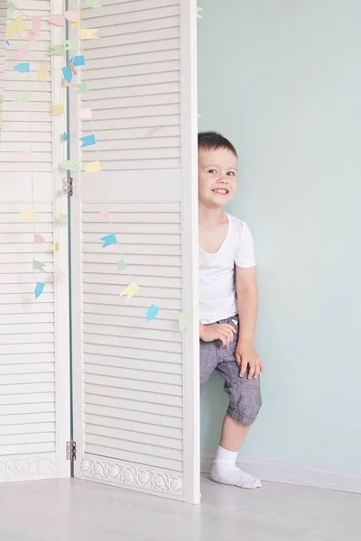 happy kid behind door. the boy plays. He hides behind the white door