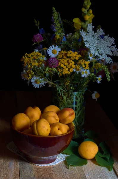 Natura morta con albicocche e un mazzo di fiori selvatici su tavole di legno, eseguite con la tecnica dell'illuminazione a bassa intensità Immagine Stock