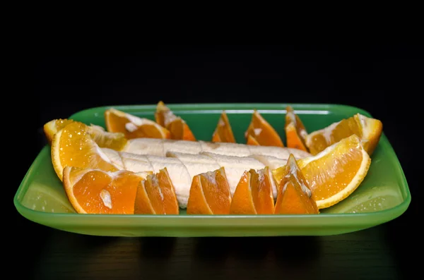 Tranches d'orange et bananes dans une assiette verte sur un dos noir — Photo