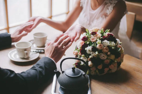 Noiva e noivo segurar as mãos um do outro. Anéis de casamento. Casal amoroso num café. chá quente para os amantes — Fotografia de Stock