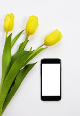 Çiçekler ve masada bir akıllı telefon. Sarı laleler, siyah smartphone