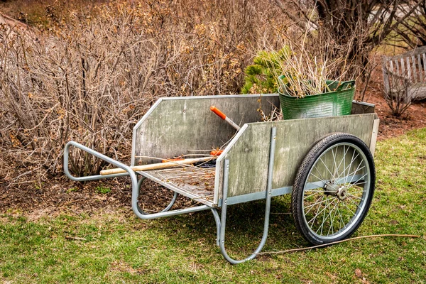 Houten tuin kar met tools en gesnoeide takken verzameld na vroege voorjaar landschapsarchitectuur opruimen — Stockfoto