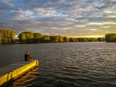 Kadın gün batımında iskelede oturuyor Illinois 'deki Fox River boyunca