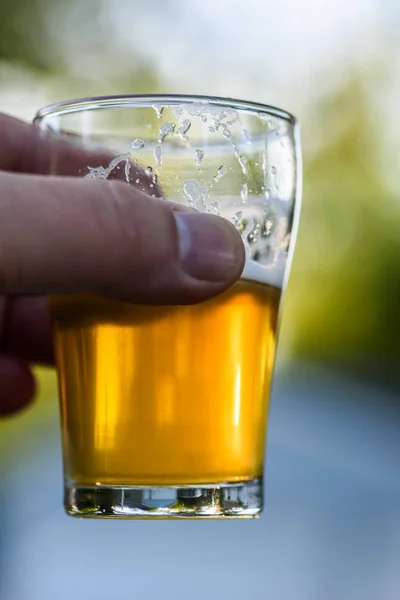 Hand hält ein kleines Glas Bier in die Höhe — Stockfoto