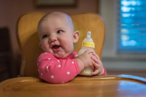 Sorrindo bebê segurando garrafa em cadeira alta — Fotografia de Stock