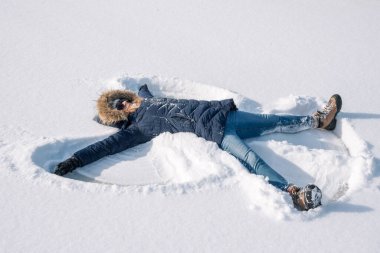 woman making a snow angel in new snow outdoors in winter clipart