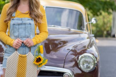 Yazın elinde ayçiçekleri olan eski model bir kamyonetin önünde duran kadının yakın çekimi.