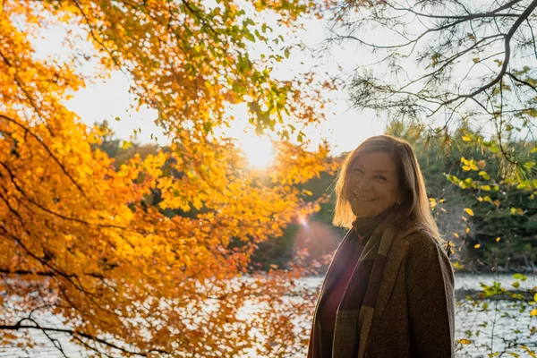 woman in scarf standing next to colorful fall leaves by lake in Autumn