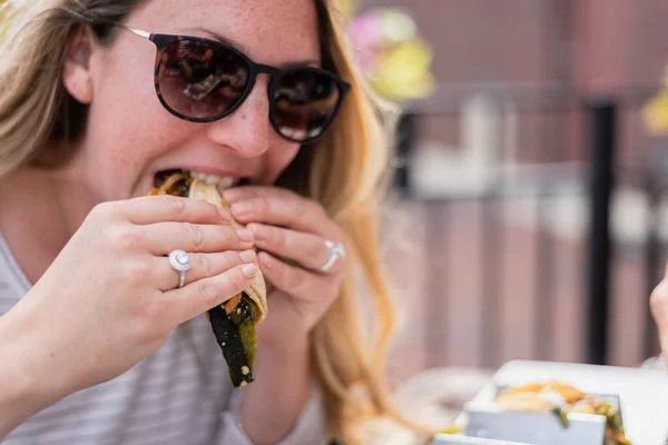 closeup of a young woman sitting outdoors eating tacos in summer