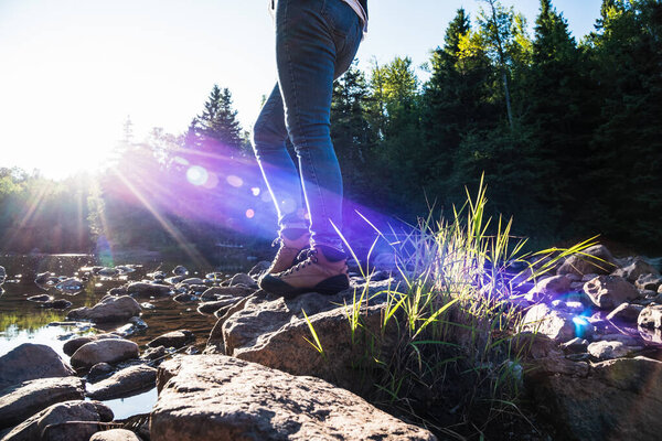woman walking across rocks on forest stream with bright sun beams