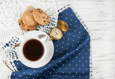 Fincan çay, kurabiye ve ahşap beyaz desenli masa saati.