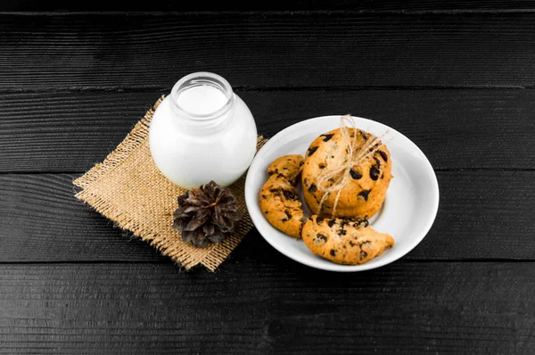 Milk, cookies on a black textured wooden table. — Stock Photo, Image