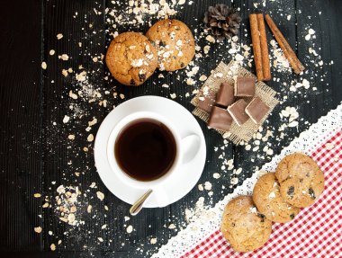 Kahve fincanı, ev yapımı yulaf ezmeli kurabiye ile kuru üzüm ve tarçın bir siyah ahşap dokulu arka plan.