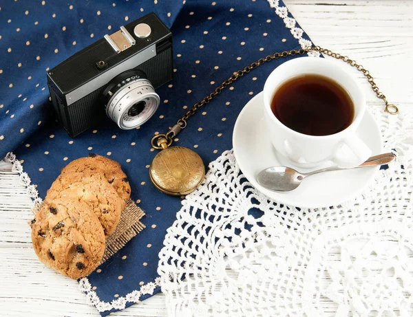 Camera, tea cup, cookies and clock on a wooden white table, vintage style. — Stock Photo, Image