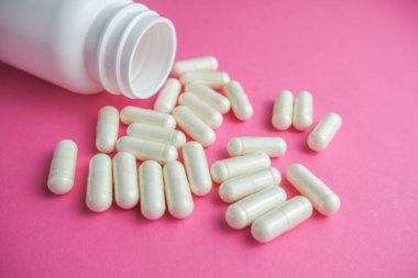 Poured pills out of the bottle on the pink background.  Concept of health, protect from viruses, flu and cold.