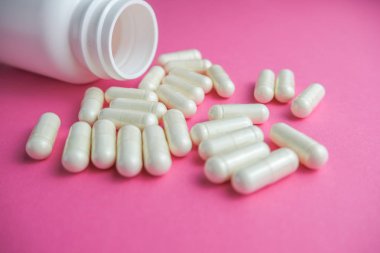 Poured pills out of the bottle on the pink background.  Concept of health, protect from viruses, flu and cold.