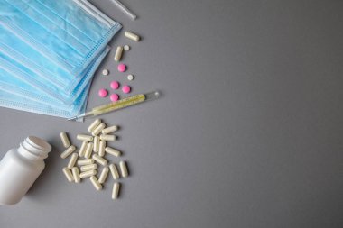 Gri arka planda termometreyi, hapları, tabletleri ve maskeleri kapatın. Virüsler, koruma, sağlık hizmetleri kavramı.