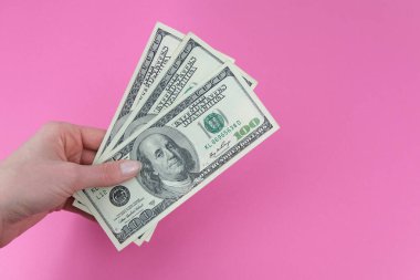 Kızın elinde para, pembe arka planda Amerikan banknotu var. Para kavramı, kazanç, vergiler, iki kez ödeme.