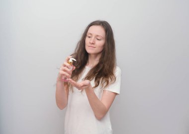 El antiseptiği tutan genç bir kız, gri bir arka planda dezenfektan.. 