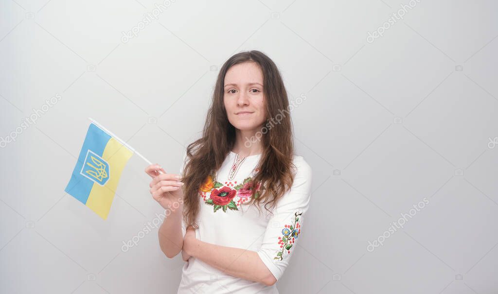 Young beautiful girl in embroidered shirt with Ukrainian flag. Attractive Ukrainian woman wearing traditional Ukrainian embroidery on the grey background. 